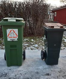 Två soptunnor står med draghandtagen vända bort från vägen. De står en bit in på vägen och med en halvmeters mellanrum. 