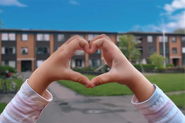 Två barnhänder som formar ett hjärta framför bostäder på Körfältet.