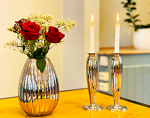 Silvervas med röda rosor och två levande ljus i silverstakar.