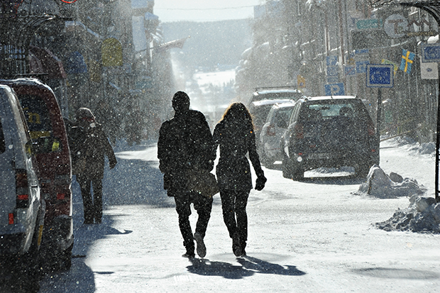 Ett par som går längs en gata med parkerade bilar på sidorna.