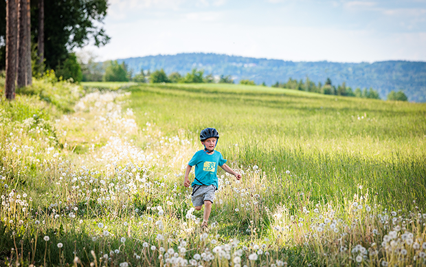 Pojke springer på en äng vid kanten av en skog.
