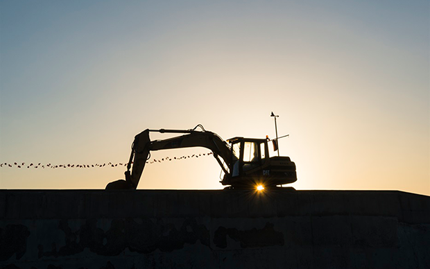 Mörk siluett av grävskopa i skymningsljus.