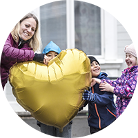 En kvinna och tre barn håller i en ballong i form av ett guldhjärta