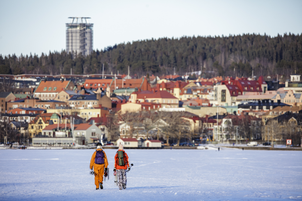 Två personer går på Storsjöns is med staden Östersund i fonden.