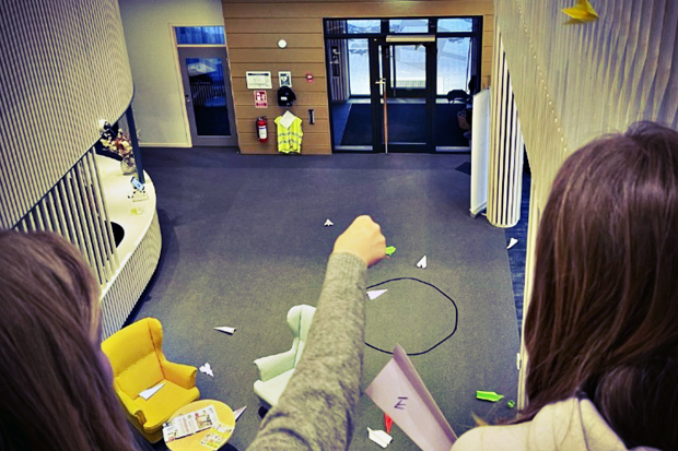 Två tjejer kastar pappersflygplan från en loftgång.