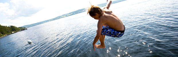 Pojke i badbyxor hoppar i sjön en solig sommardag