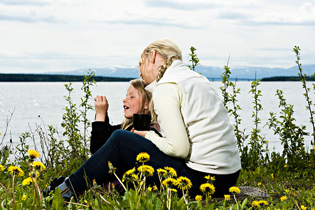 En kvinna och en flicka som sitter tillsammans i gräset med Storsjön och fjällen i bakgrunden