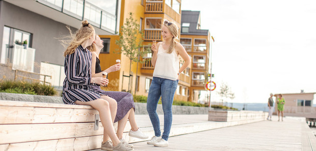 Tre glada tjejer pratar längs Storsjö strand med höghus i bakgrunden