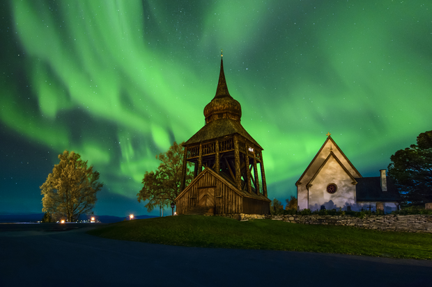 En klockstapel och kyrka med norrsken i bakgrunden