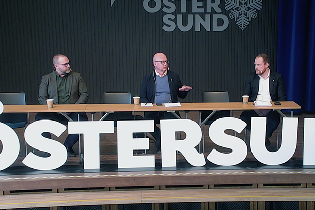 Tre personer sittande vid ett podium med ordet "Östersund" i stora bokstäver framför