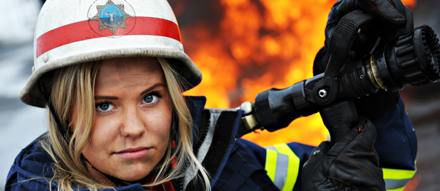 Kvinnlig brandman i förgrunden med en brand i bakgrunden