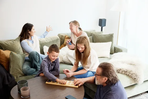 Personer i olika åldrar umgås och spelar spel tillsammans i ett vardagsrum.