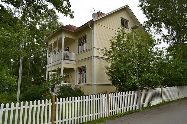 Majsen 4, Villa med gul liggande träpanel, balkong och röda fönster.