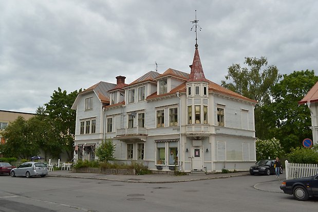 Nejlikan 11. Flerbostadshus i tre våningar, ljusblå, liggande träpanel och vita fönster med spröjs. Ett torn i höger hörn och rött plåttak.