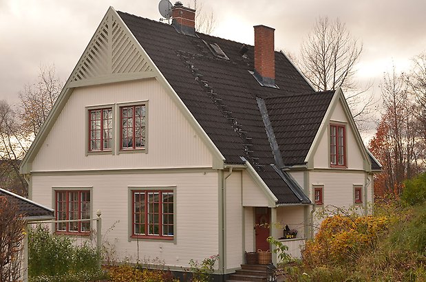 Solskiftet 12. Villa i vit, liggande panel med gröna detaljer och röda fönster med spröjs.