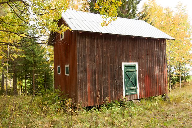 Byggnad med mörkröd panel med grön dörr och tre små fönster på kortsidan.