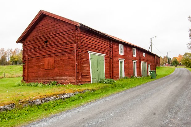 Stor timrad byggnad i rött med gröna dörrar och fönster med via spröjs.