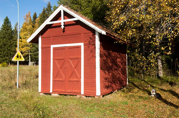 Liten byggnad i röd panel med vita knutar och röda portar.