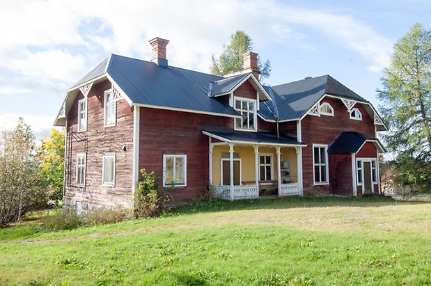 Stort rött hus i två våningar med fönster med vita spröjs och gulmålad förstukvist.