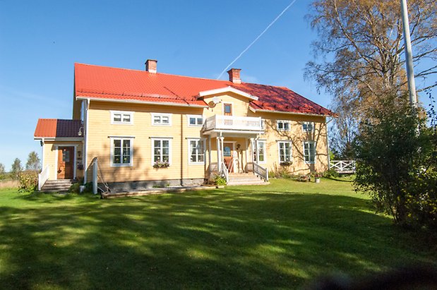 Fjäl 4:34. Villa i gul liggande panel med förstukvist och balkong, Bruna dörrar och fönster med vita spröjs.