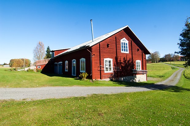 Handog 6:4. Timrad, rödmålad ladugård med fönster med vita spröjs och tre blå dörrar.