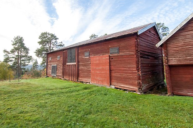 Hölje 3:4. Timrad, röd byggnad med svarta luckor.