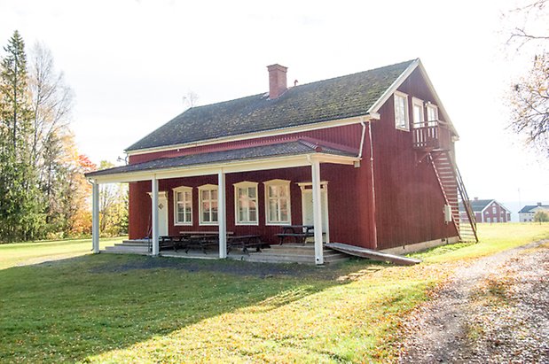 Hölje 3:9. Hus i två våningar i röd panel med fönster med vita spröjs och skärmtak längs långsidan.