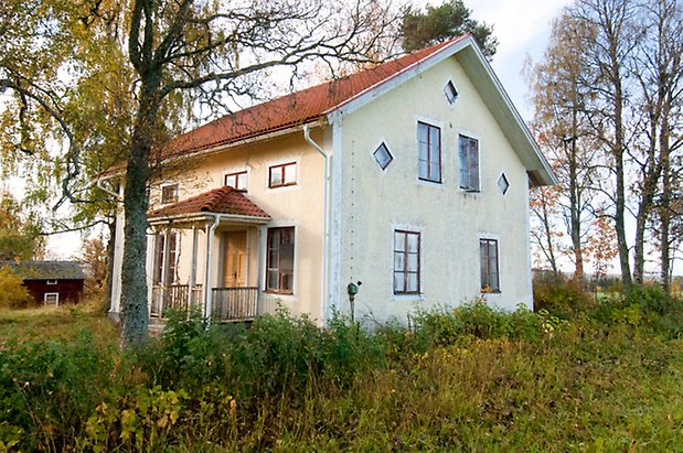 Hölje 4:7. Villa i tre våningar i ljusgul puts med förstukvist och fönster med röda spröjs. 