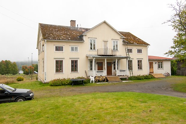 Klösta 3:2. Villa i tre våningar i ljusgul panel med förstukvist och balkong i svart smide, fönster med röd spröjs. 