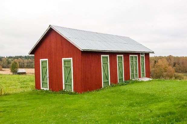 Korsta 2:15. Byggnad i röd panel med sju gröna portar.