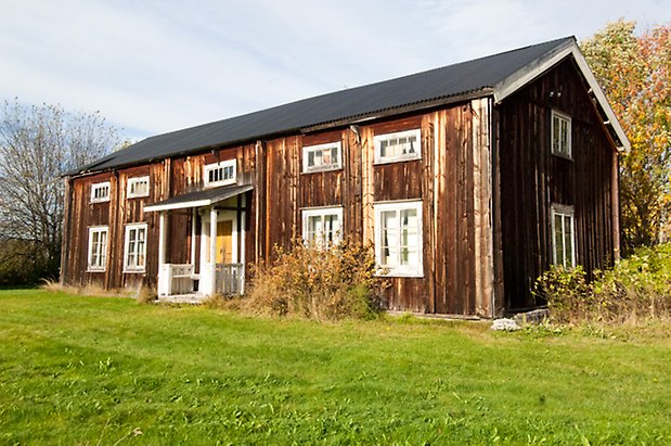 Lits-Åsen 2:9. Hus i två våningar i brun panel med vit förstukvist med gul dörr och fönster med vita spröjs.