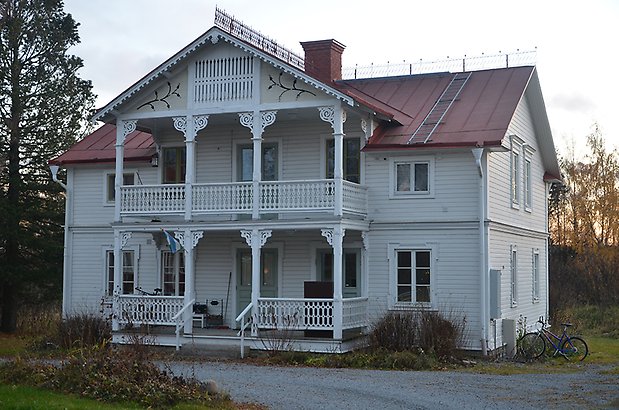 Stallet 7. Villa med vit liggande panel med veranda och balkong med snickarglädje.