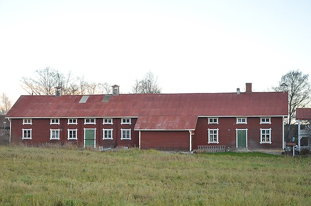 Stallet 7. Lång röd byggnad med vita fönster med spröjs och gröna dörrar.