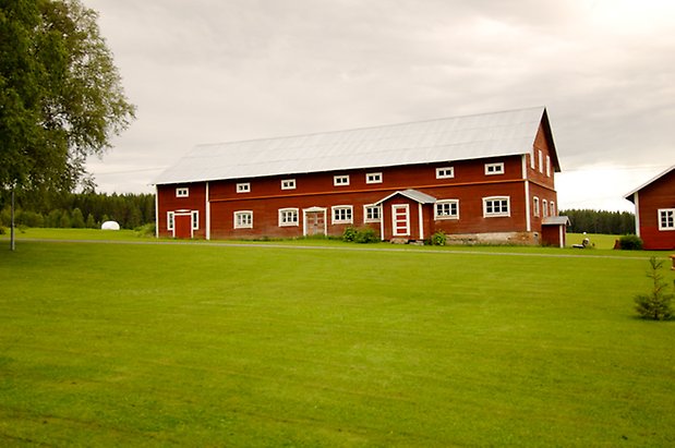 Digernäs 2:7. Ladugård i rött timmer i två våningar, med fönster med vita spröjs, två dubbelportar i rött, och dörr i rött/vitt.