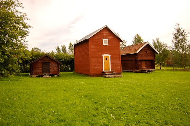 Fannbyn 6:9. Byggnad i två våningar i röd, liggande panel med gul dörr och ett litet fönster med spröjs.