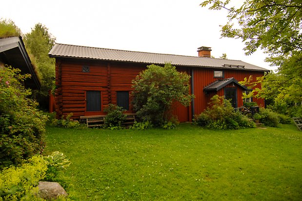 Hara 8:3. Timrad, röd byggnad med två svarta luckor, hopbyggd med en byggnad i röd panel med svart dörr.