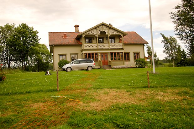 Åkeräng 2:14. Villa i två våningar i ljusgrön, liggande panel med gröna och röda detaljer. Punschveranda med balkong ovanför med balkong med snickarglädje.