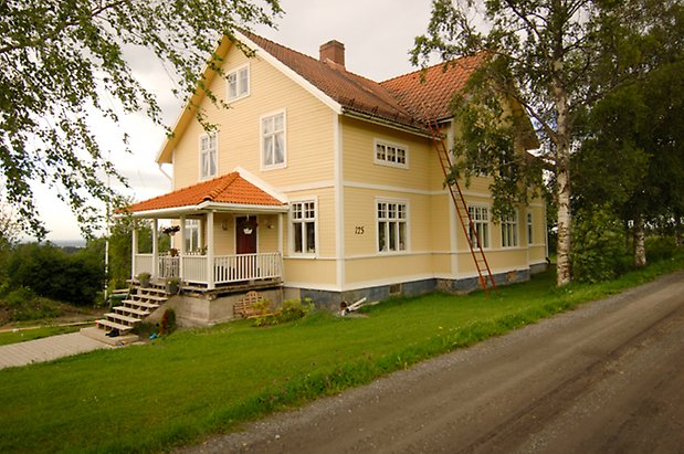 Åkeräng 3:3. Villa i tre våningar i ljusgul, liggande panel med förstukvist på kortsidan och fönster med vita spröjs.