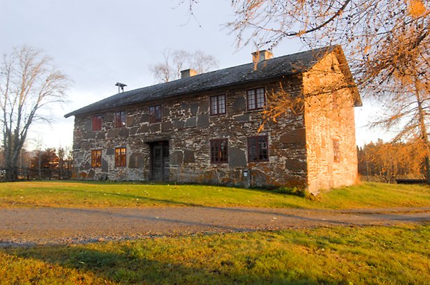 Näs-Bleka 1:10. Byggnad i två våningar i sten med svart dubbelport och fönster med spröjs, två skorstenar och en ställning med klocka på taket.