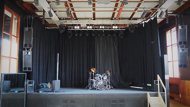 Scenen i tingssalen med ett trumset och till vänster om trummorna en ljudanläggning.Till vänster i bild ser man en bit av en spegel och till höger en trapp som går upp på scenen