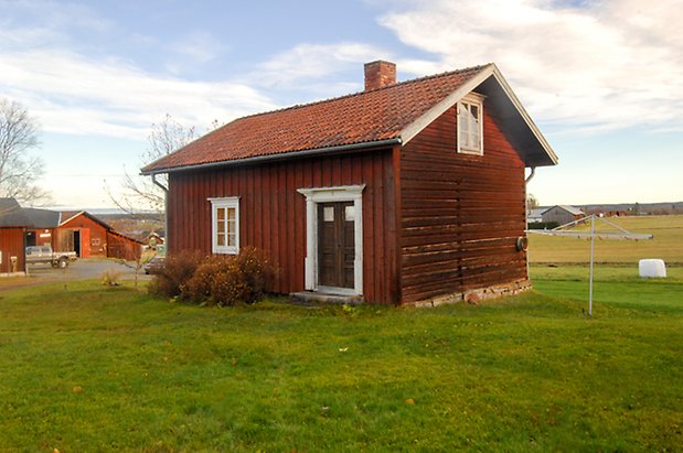 Öd 2:2. Litet hus med timmer och panel i två våningar, fönster med vita spröjs, svarta dubbeldörrar.