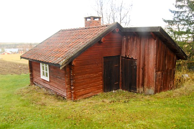 Öd 2:2. Röd, timrad byggnad med fönster med vita spröjs och svart port, tillbyggnad i vinkel i panel med svart port.