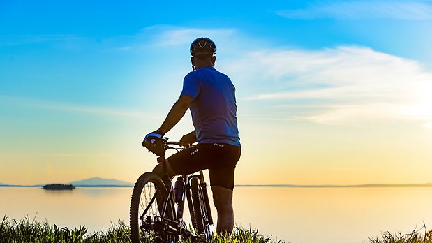 En cyklist tittar ut över Storsjön och vacker solnedgång