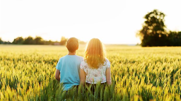Två barn sitter med ryggen mot kameran i ett gräsfält