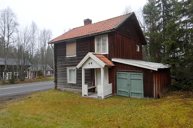 Kläppe 3:8. Hus i två våningar i timmer och panel, fönster med vita spröjs, vit förstukvist, ett fönster täckt med plywood, tillbyggnad på kortsidan med grå dubbelport.