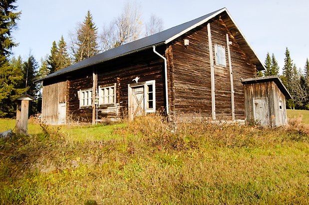 Österåsen 5:5. Byggnad i brunt timmer, fönster med vita spröjs, port. Tillbyggt dass på kortsidan.