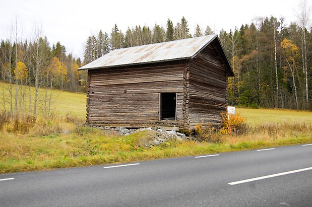 Häggesta 1:104. Byggnad i grått timmer med öppen lucka.