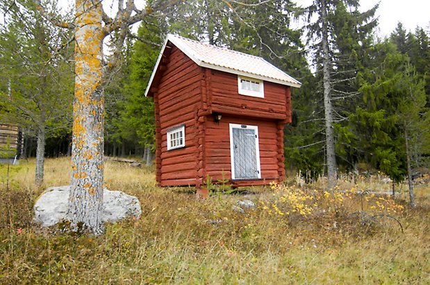 Lassgård 2:1. Rött, timrat härbre med blå lucka, fönster med vita spröjs.