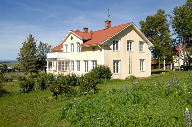 Glasätt 1:7. Villa i ljusgul panel med vita detaljer, fönster med vita spröjs, inglasad veranda med balkong ovanför.