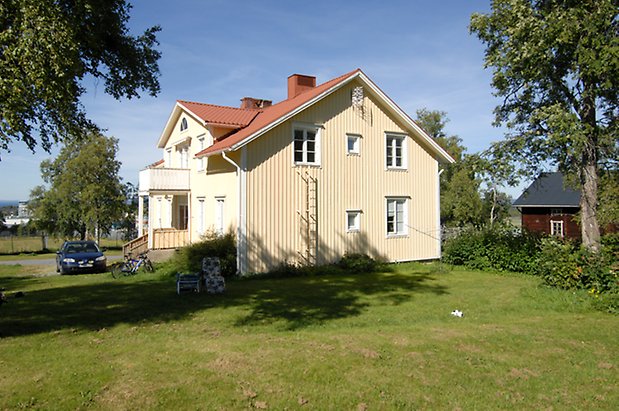 Glasätt 1:7. Villa i ljusgul panel med vita detaljer, fönster med vita spröjs, förstukvist med balkong ovanför.